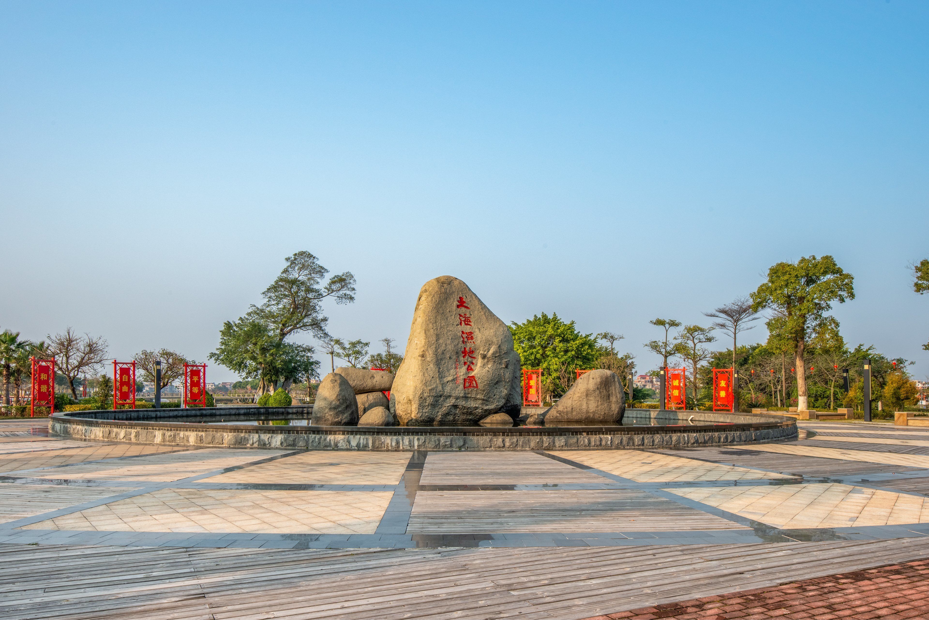 A large rock formation with inscriptions, surrounded by a tiled plaza with red banners.
