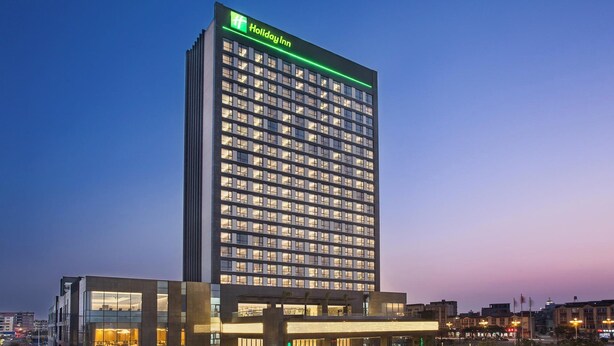 A tall, modern Holiday Inn hotel building with a prominent green sign at the top. - Holiday Inn Putian Xiuyu by IHG (Putian)