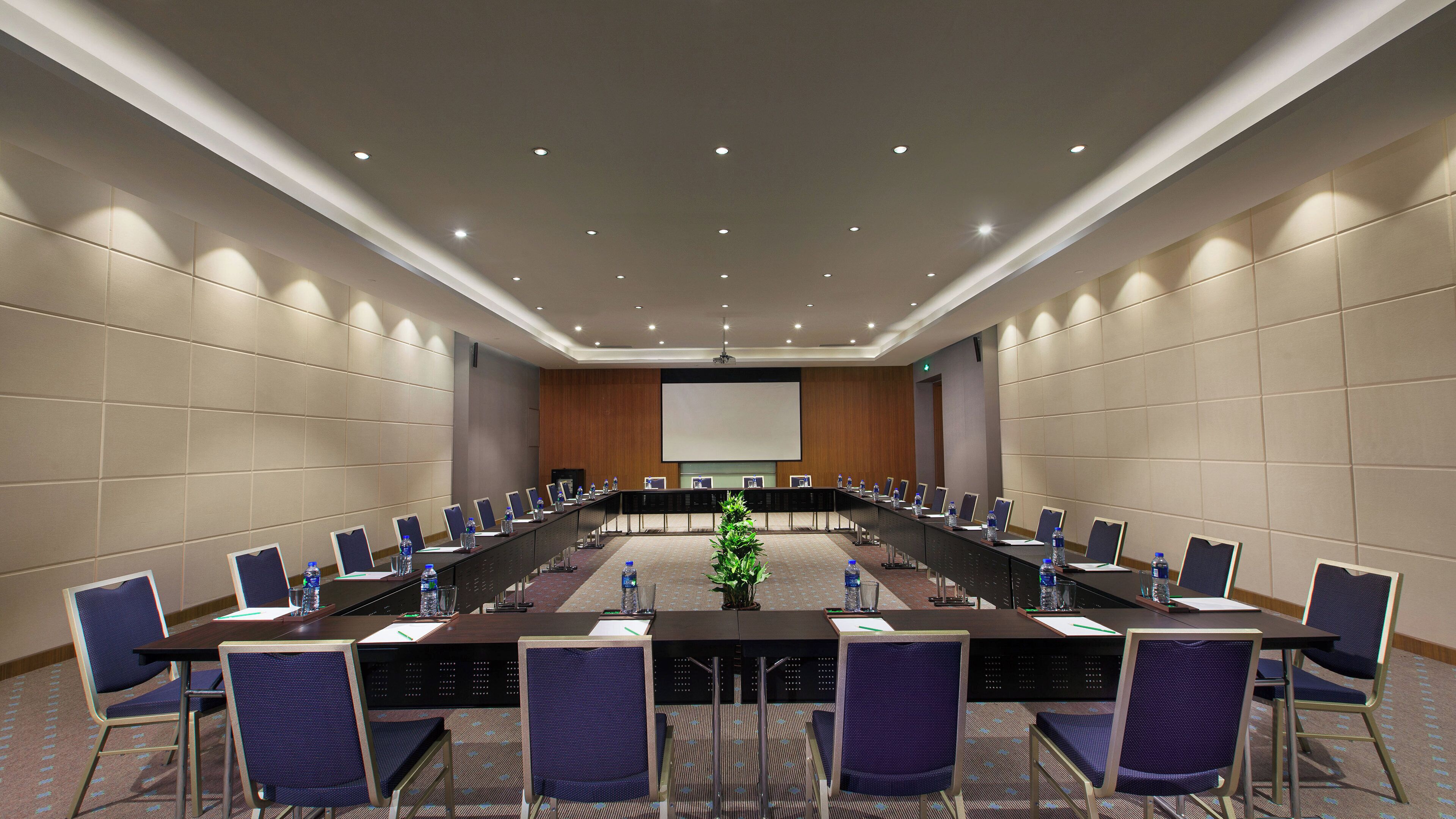 A conference room with a long table, chairs, and a projector screen.