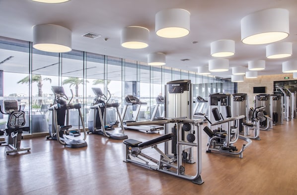 Un gimnasio con máquinas de cardio, estaciones de pesas y amplias ventanas con vistas a palmeras.
