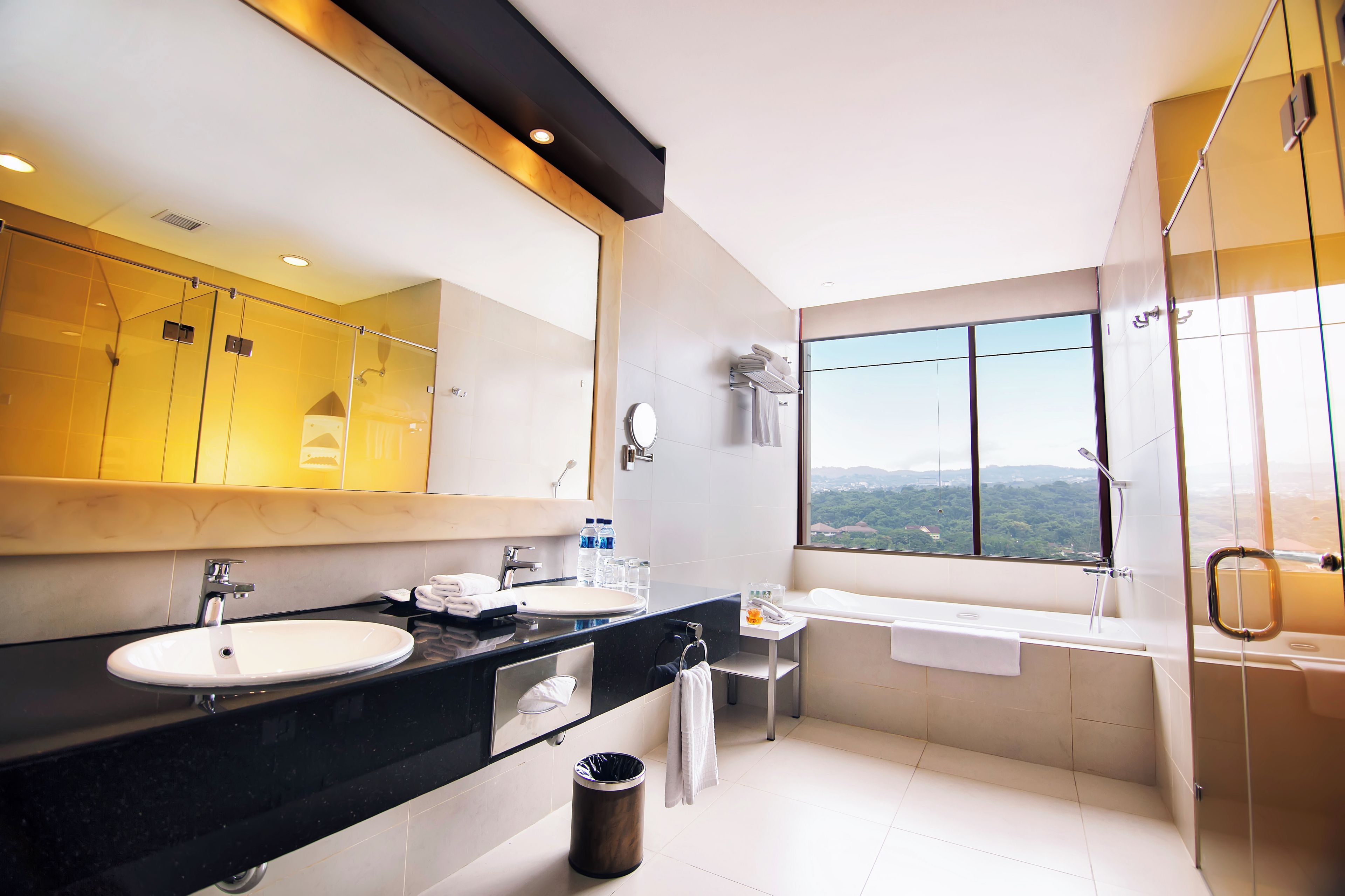 A modern bathroom with a large mirror, two sinks, a bathtub, and a shower.