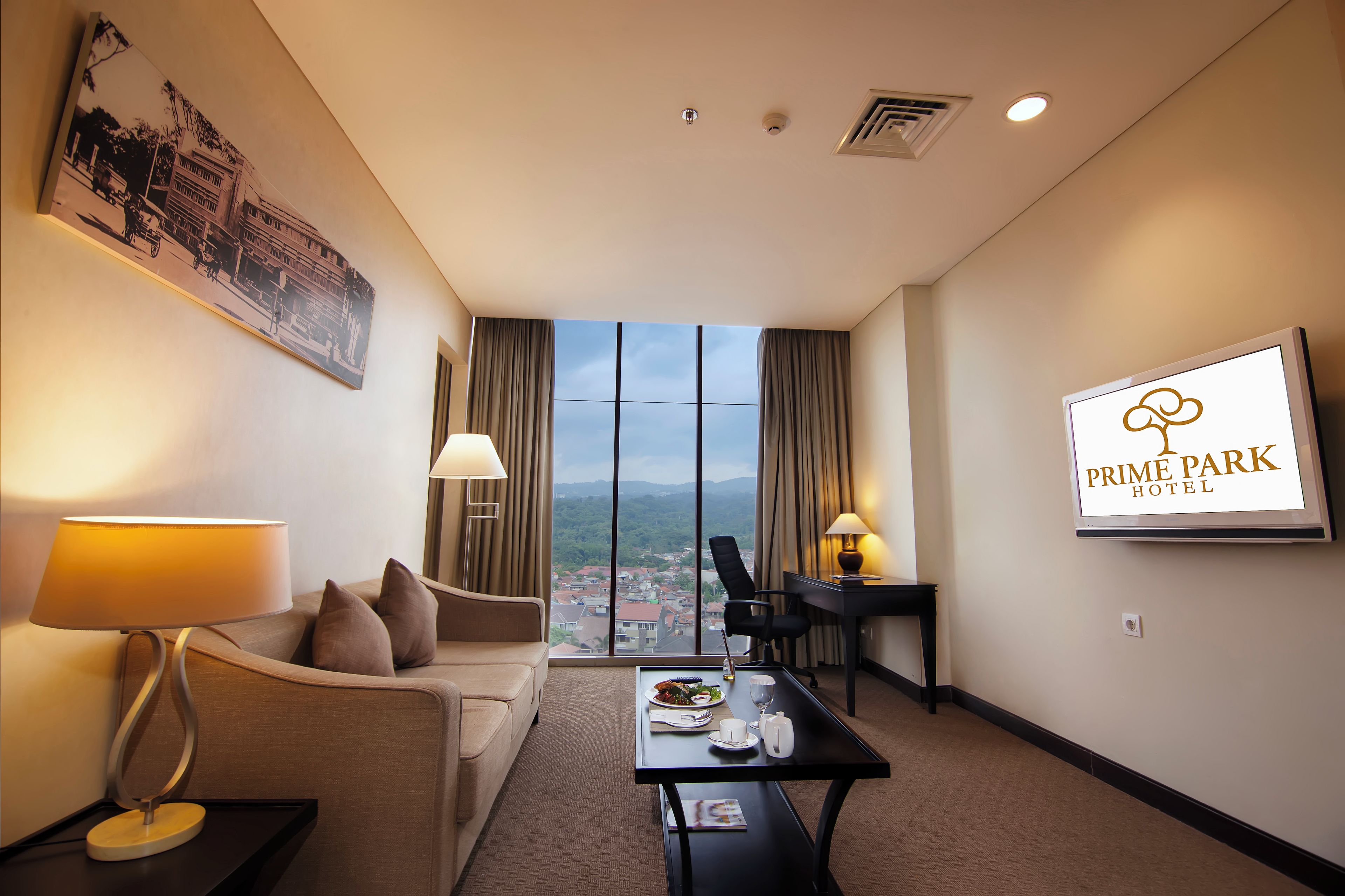 A hotel room with a large window, a desk, a chair, a sofa, and a dining table with a meal set.
