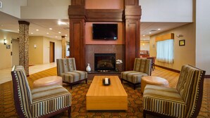 A lobby with a fireplace, four striped armchairs, a coffee table, and a television. - Best Western Plus Finger Lakes Inn & Suites (Cortland)