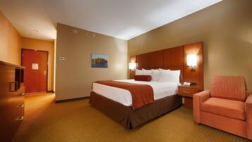 A hotel room with a bed, a nightstand, a chair, a desk, and a door.