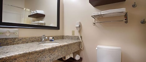 A bathroom with a granite countertop sink, a mirror, a hairdryer, and a toilet.