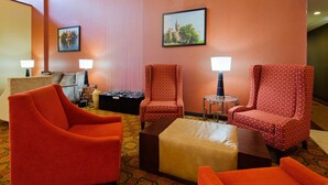 A hotel lobby with red patterned chairs, a brown ottoman, and two lamps on a round table. - Best Western Plus Finger Lakes Inn & Suites (Cortland)