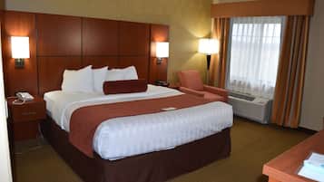 Een hotelkamer met een groot bed, twee bedlampen, een bureau en een raam met gordijnen.