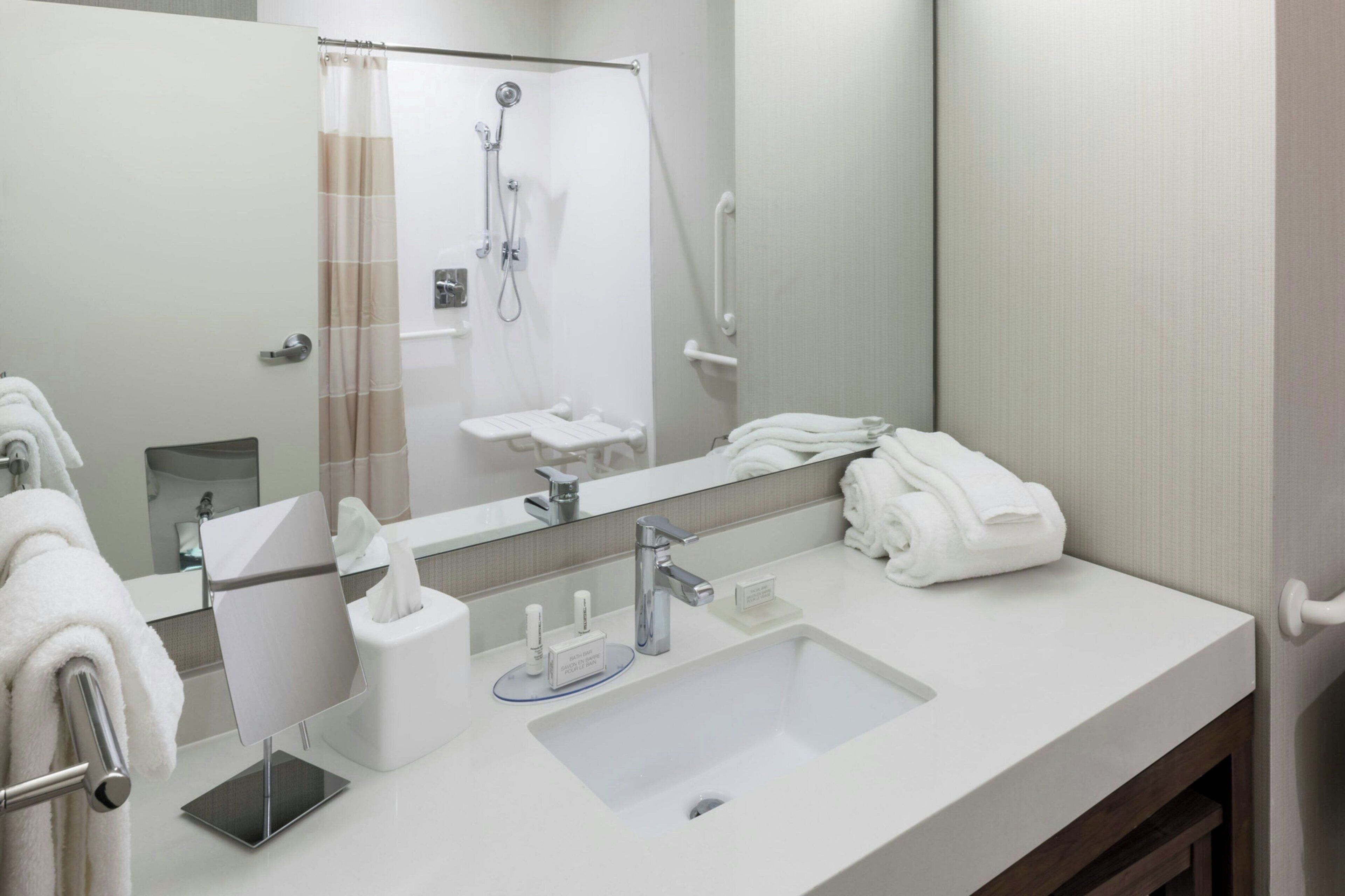A modern bathroom with a large mirror, a sink, a shower, and a towel rack.