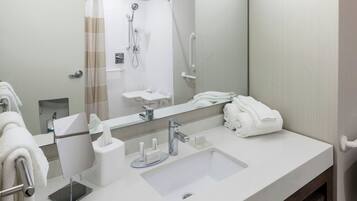 A modern bathroom with a large mirror, a sink, a shower, and a towel rack.