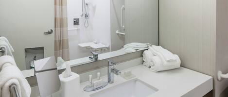 A modern bathroom with a large mirror, a sink, a shower, and a towel rack.