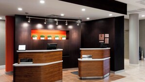 A reception area with two wooden reception desks, a digital display, and a wall-mounted plant shelf. - Courtyard by Marriott Houston North/Shenandoah (Shenandoah)