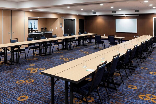 A conference room with long tables, chairs, a projector screen, and a carpeted floor. - Courtyard by Marriott Houston North/Shenandoah (Shenandoah)