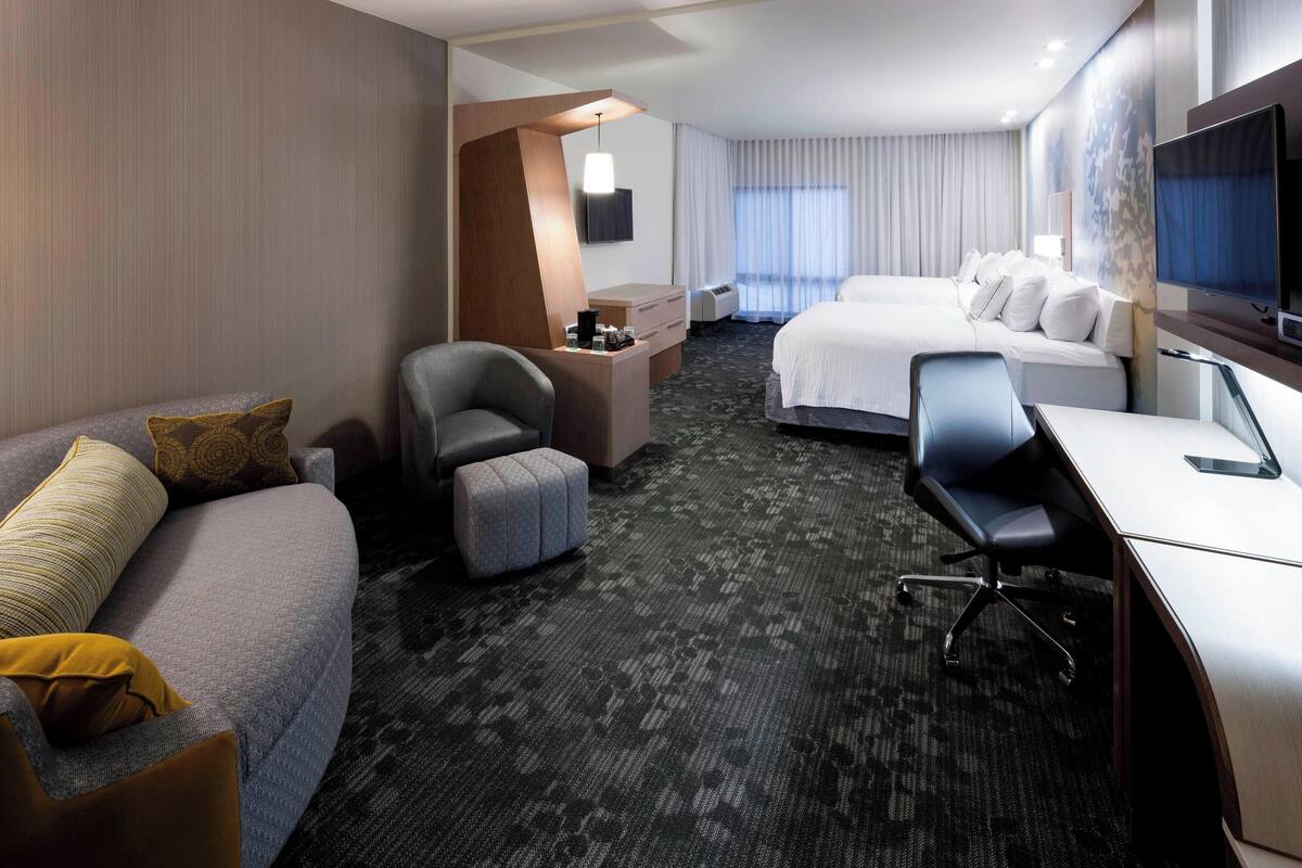 A hotel room with a sofa, a desk, a chair, a bed, and a TV.