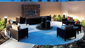 An outdoor patio with wicker furniture, a stone wall, and a built-in fireplace. - Courtyard by Marriott Houston North/Shenandoah (Shenandoah)