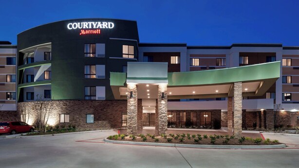 A Courtyard Marriott hotel with a curved facade, stone pillars, and a landscaped entrance area. - Courtyard by Marriott Houston North/Shenandoah (Shenandoah)