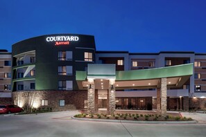 A Courtyard Marriott hotel with a curved facade, stone pillars, and a landscaped entrance area. - Courtyard by Marriott Houston North/Shenandoah (Shenandoah)
