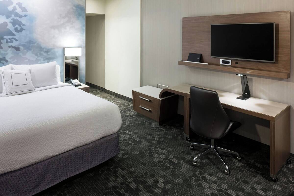 A hotel room with a large bed, a desk with a chair, a flat-screen TV, and a mirror.