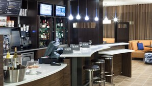 A modern bar area with a curved counter, bar stools, and a seating area with a sofa and a small table. - Courtyard by Marriott Houston North/Shenandoah (Shenandoah)