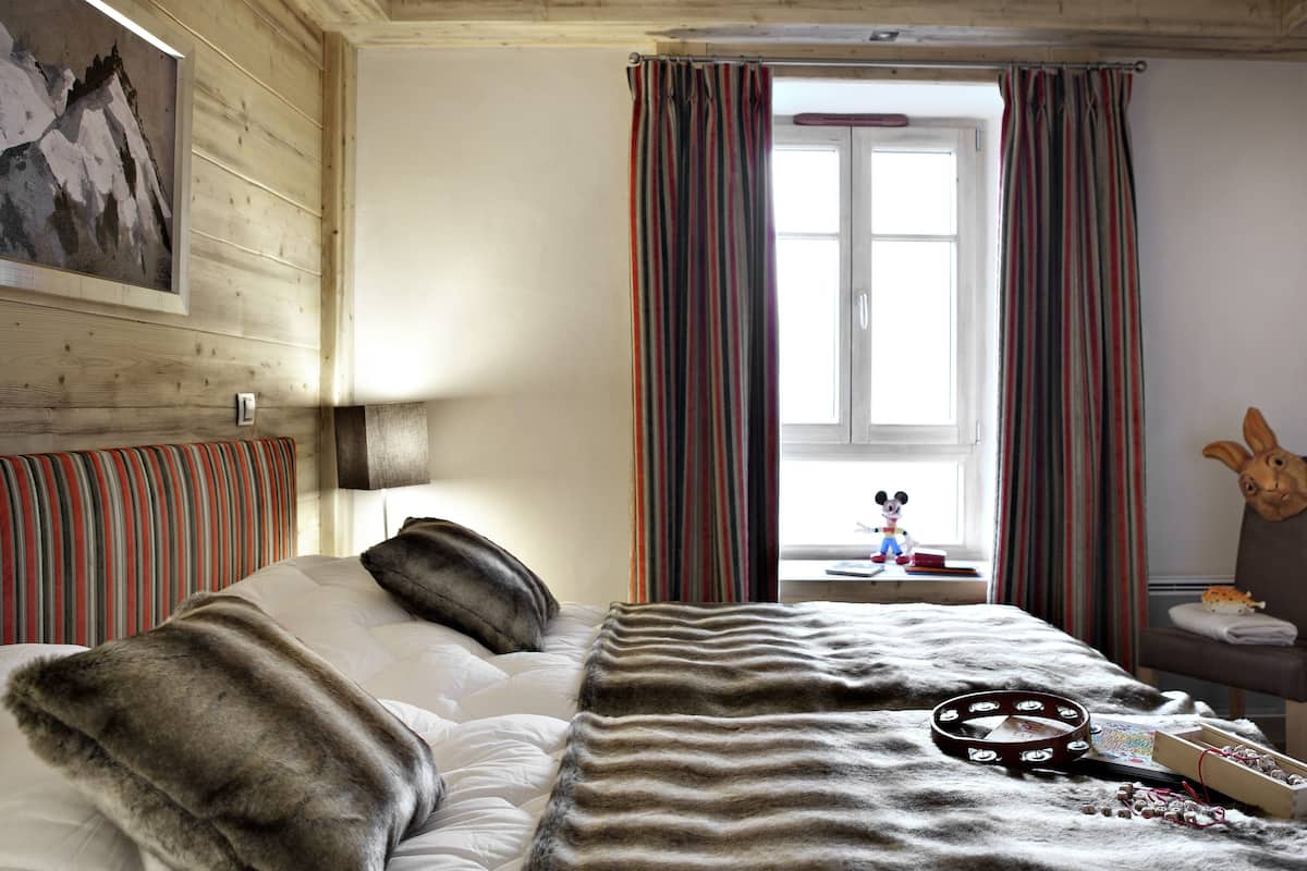 A room with a bed, a window with curtains, a headboard, and a wall-mounted picture.