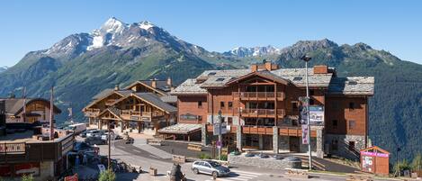 A mountain resort with wooden buildings, a ski lift, and a view of snow-capped peaks.