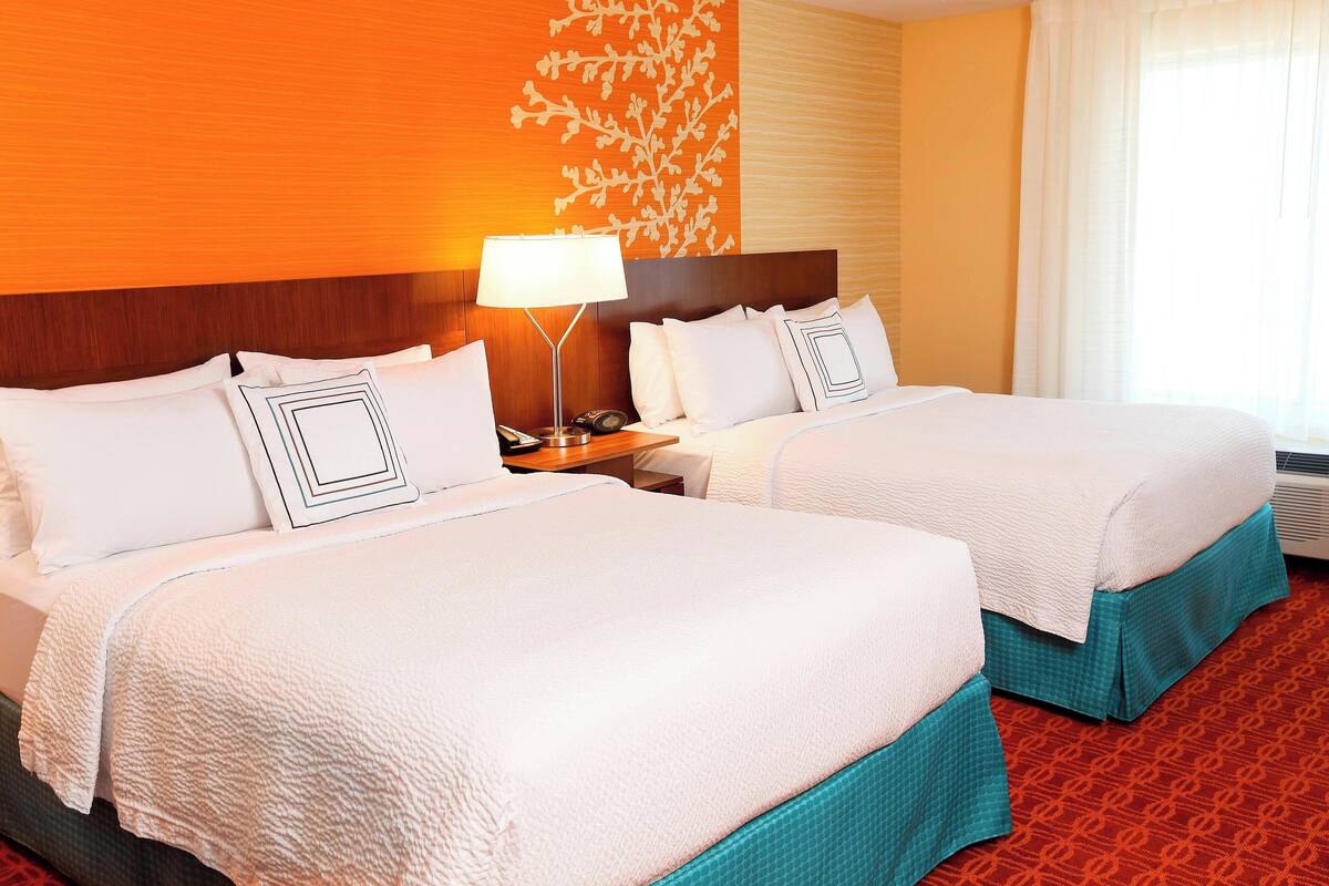 A hotel room with two beds, a nightstand, a lamp, and a wall with a leaf pattern.