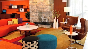 Un hall d’hôtel moderne avec une cheminée en pierre, un canapé rouge, un fauteuil en cuir marron et une table basse ronde.
