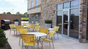 Une terrasse extérieure avec des chaises et des tables jaunes, un bâtiment en pierre et un barbecue.