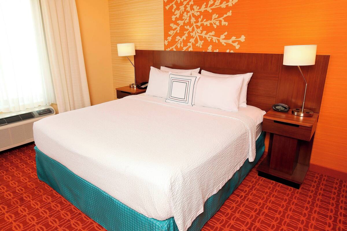 A hotel room with a large bed, a wooden headboard, two bedside tables with lamps, and a patterned carpet.