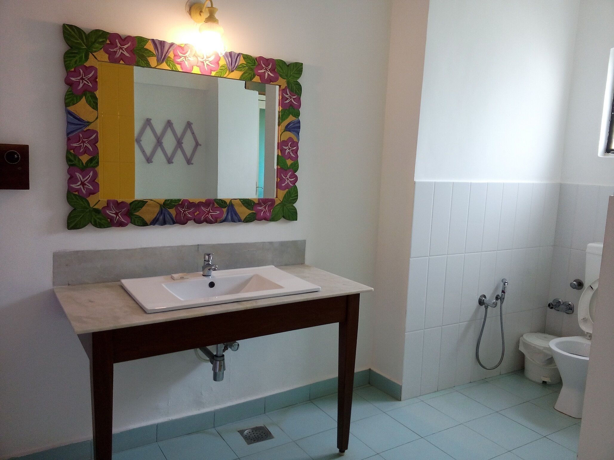 Une salle de bain avec un lavabo blanc, un miroir orné d’un cadre floral et des toilettes.