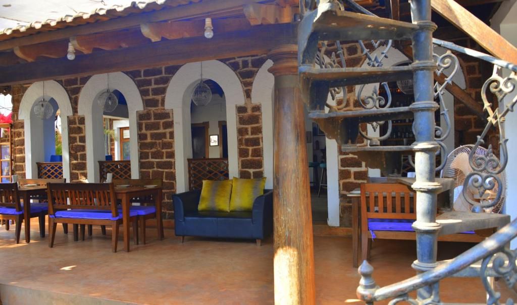 Una habitación con un sofá azul, sillas de madera y una escalera con barandales de metal ornamentados.