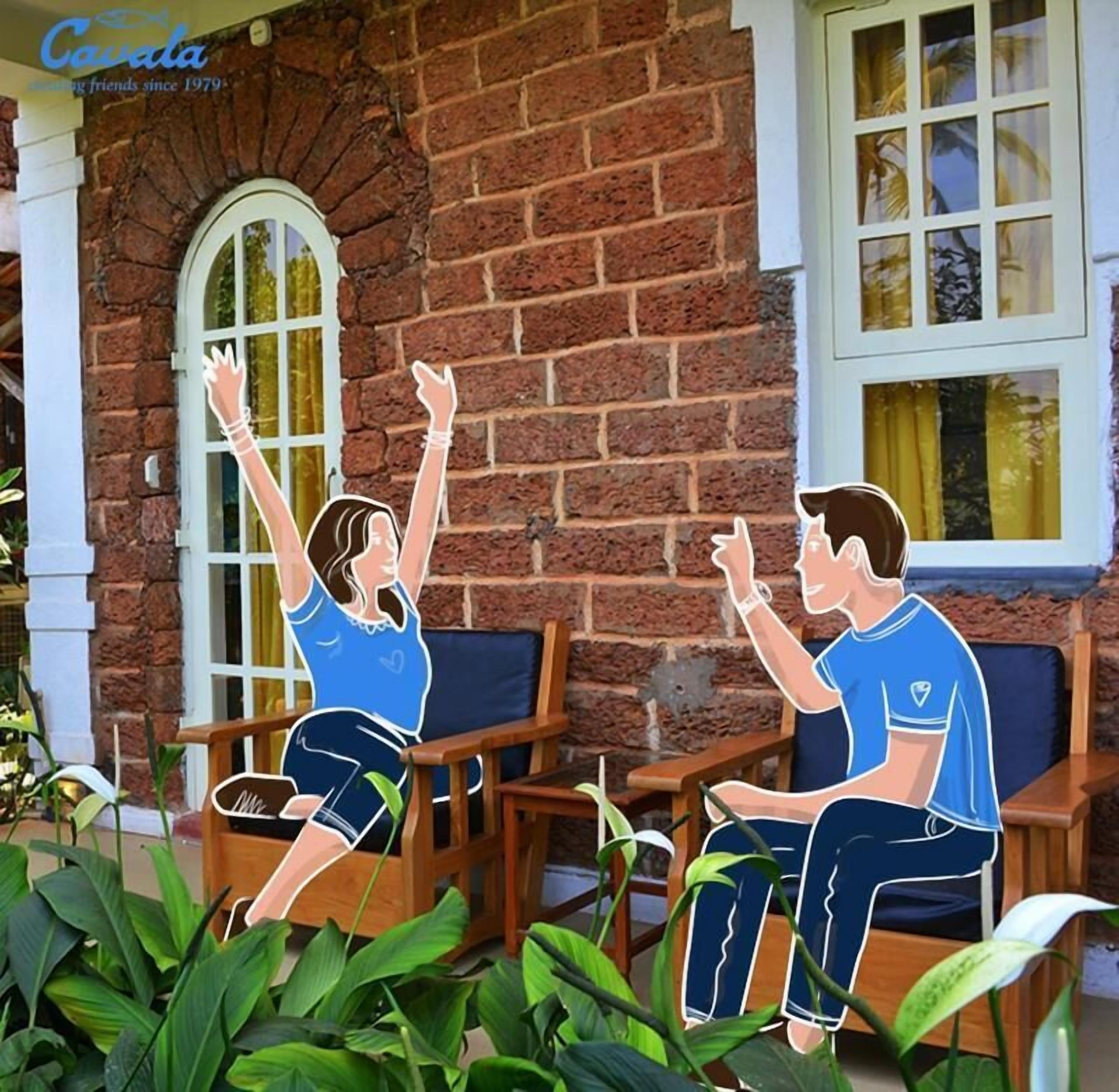 Two people sitting on wooden chairs in front of a brick building with a window and a door.