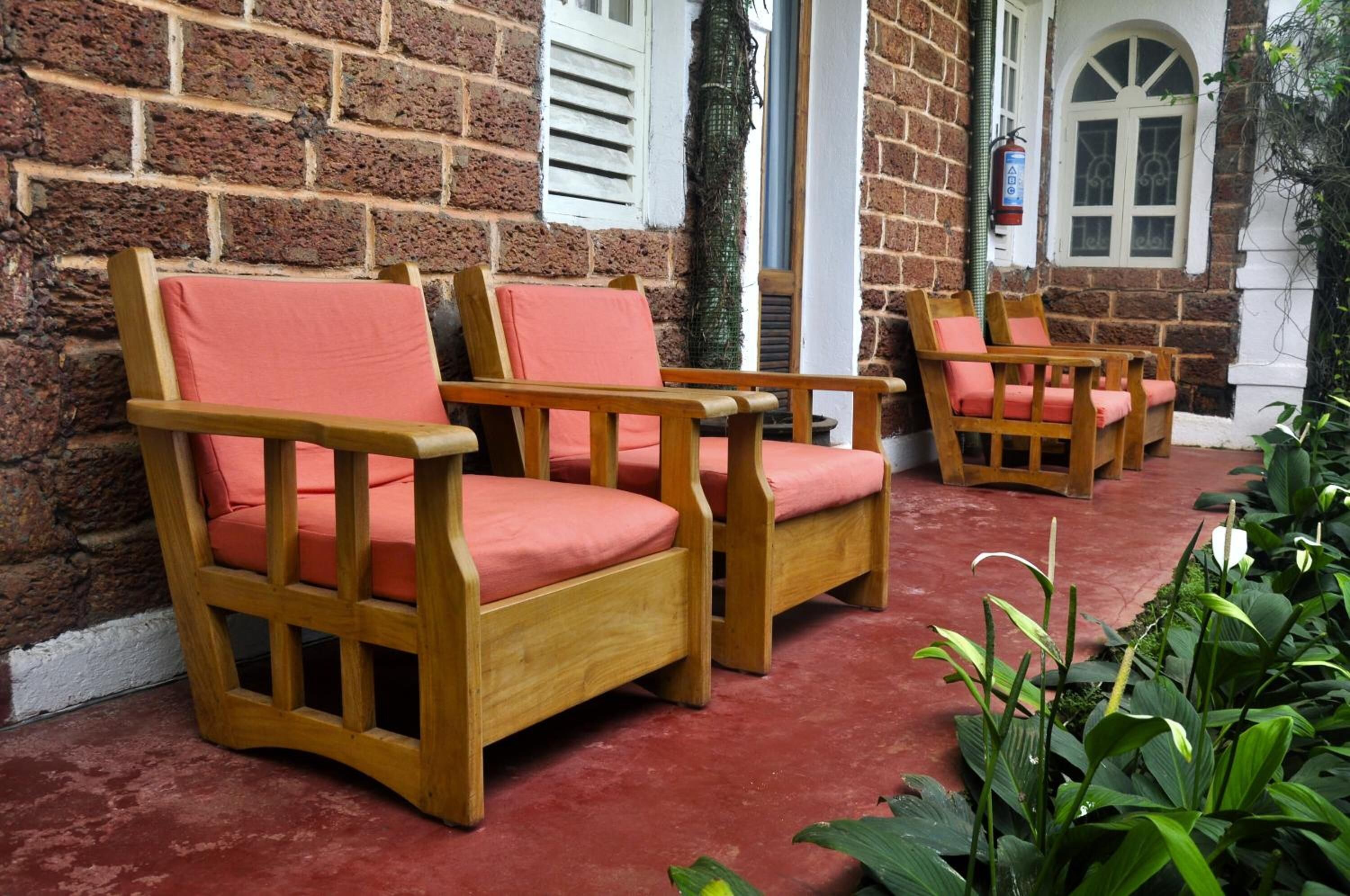 Two wooden chairs with red cushions, a brick wall, and a window with white shutters.