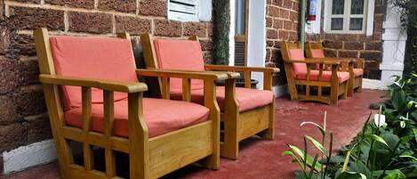 Two wooden chairs with red cushions, a brick wall, and a window with white shutters.