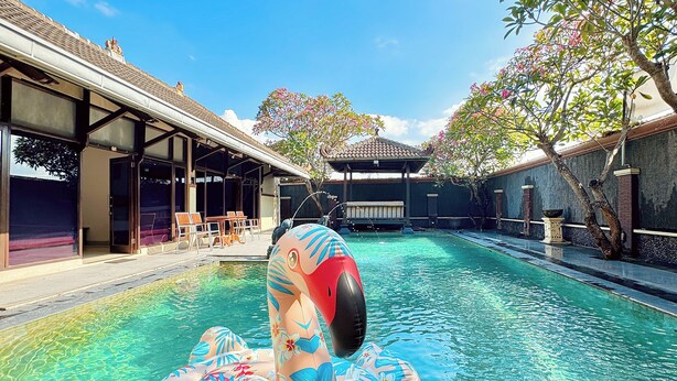 A swimming pool with a flamingo float, a covered seating area, and a building with a tiled roof. - Chrome Hotel & Resort Solo (Colomadu)