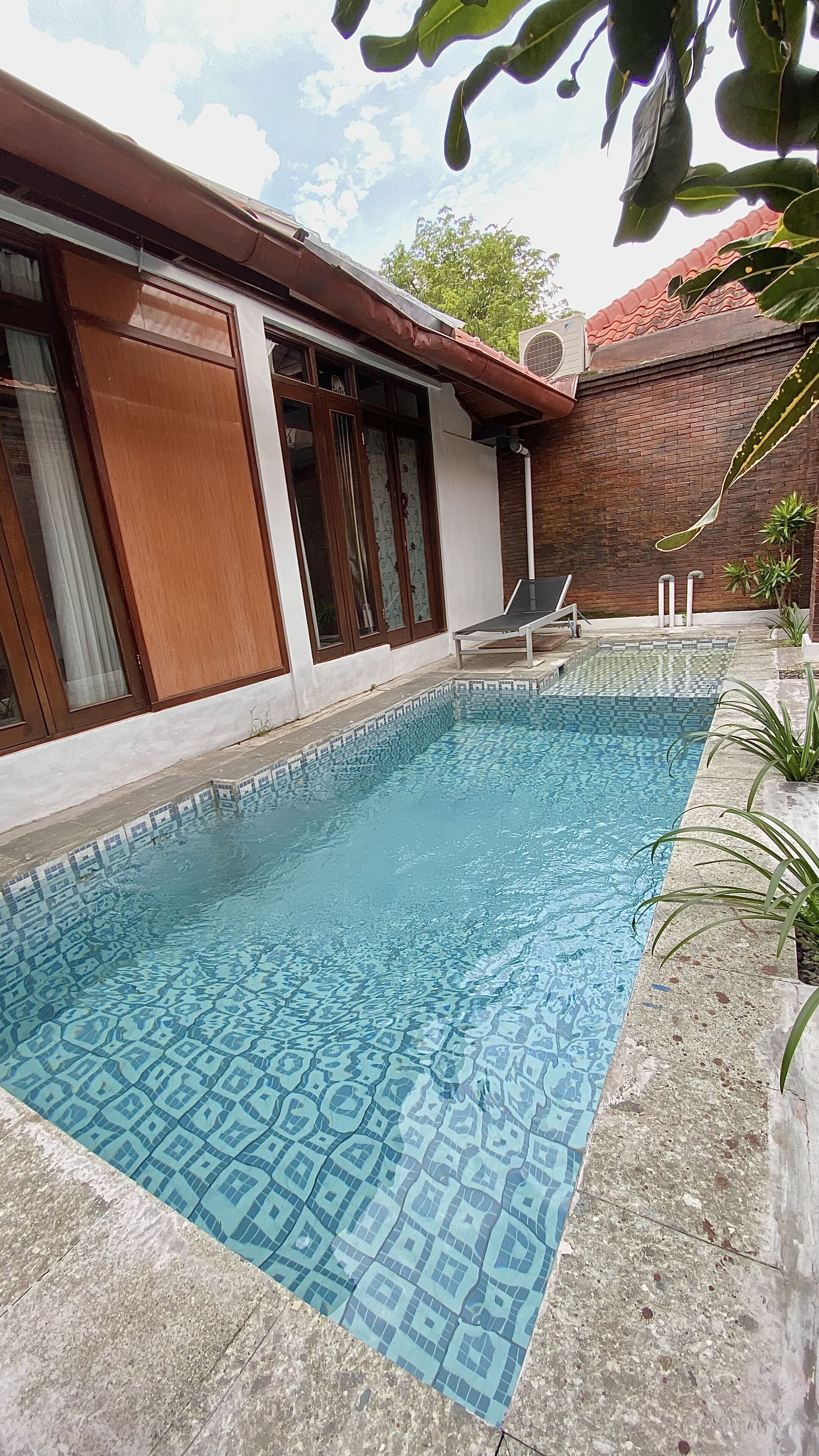 A swimming pool with a geometric tile pattern, surrounded by a brick wall and a wooden deck.