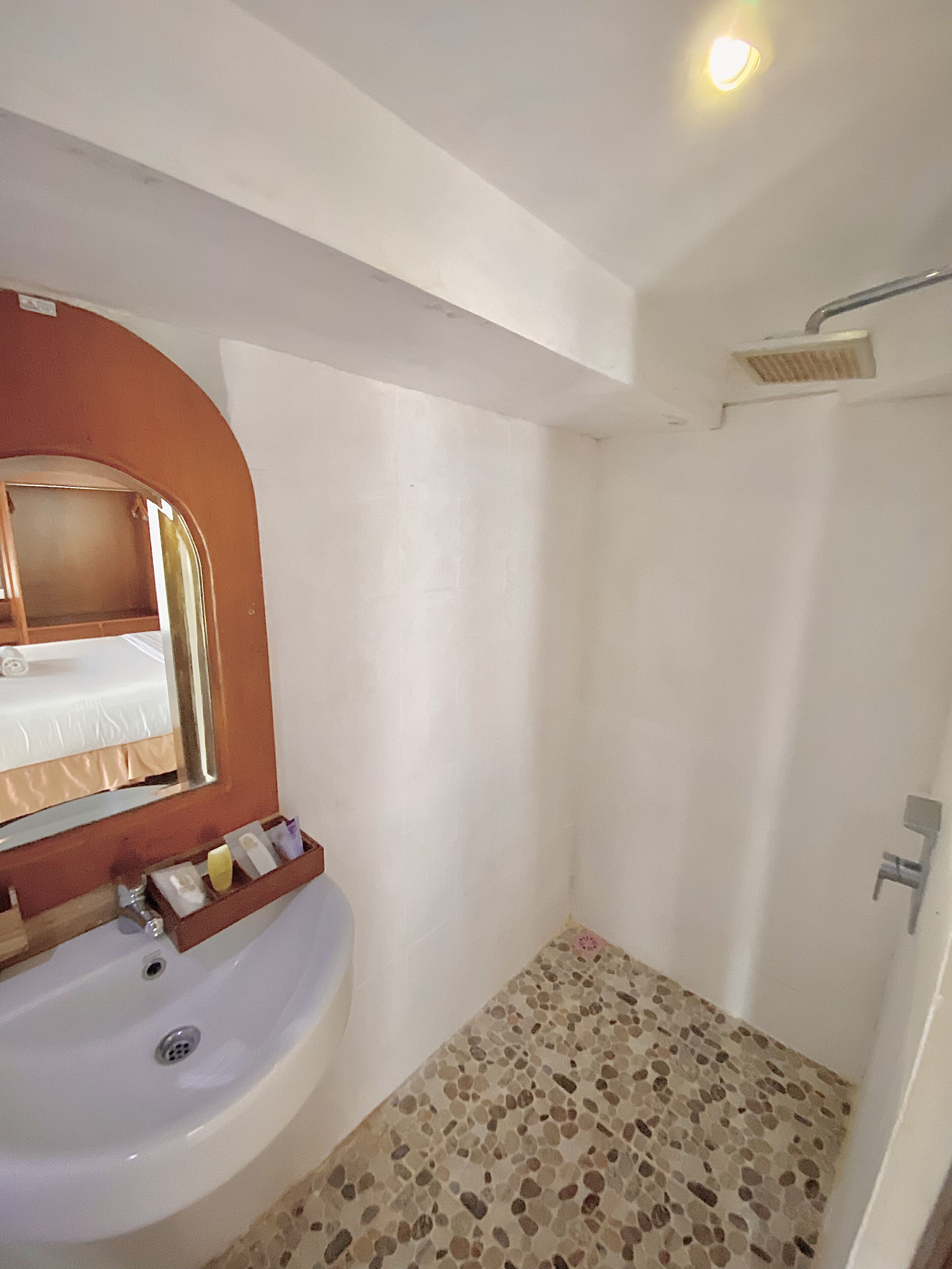 Een badkamer met een wit wastafelmeubel, een spiegel, een douche en een betegelde vloer.