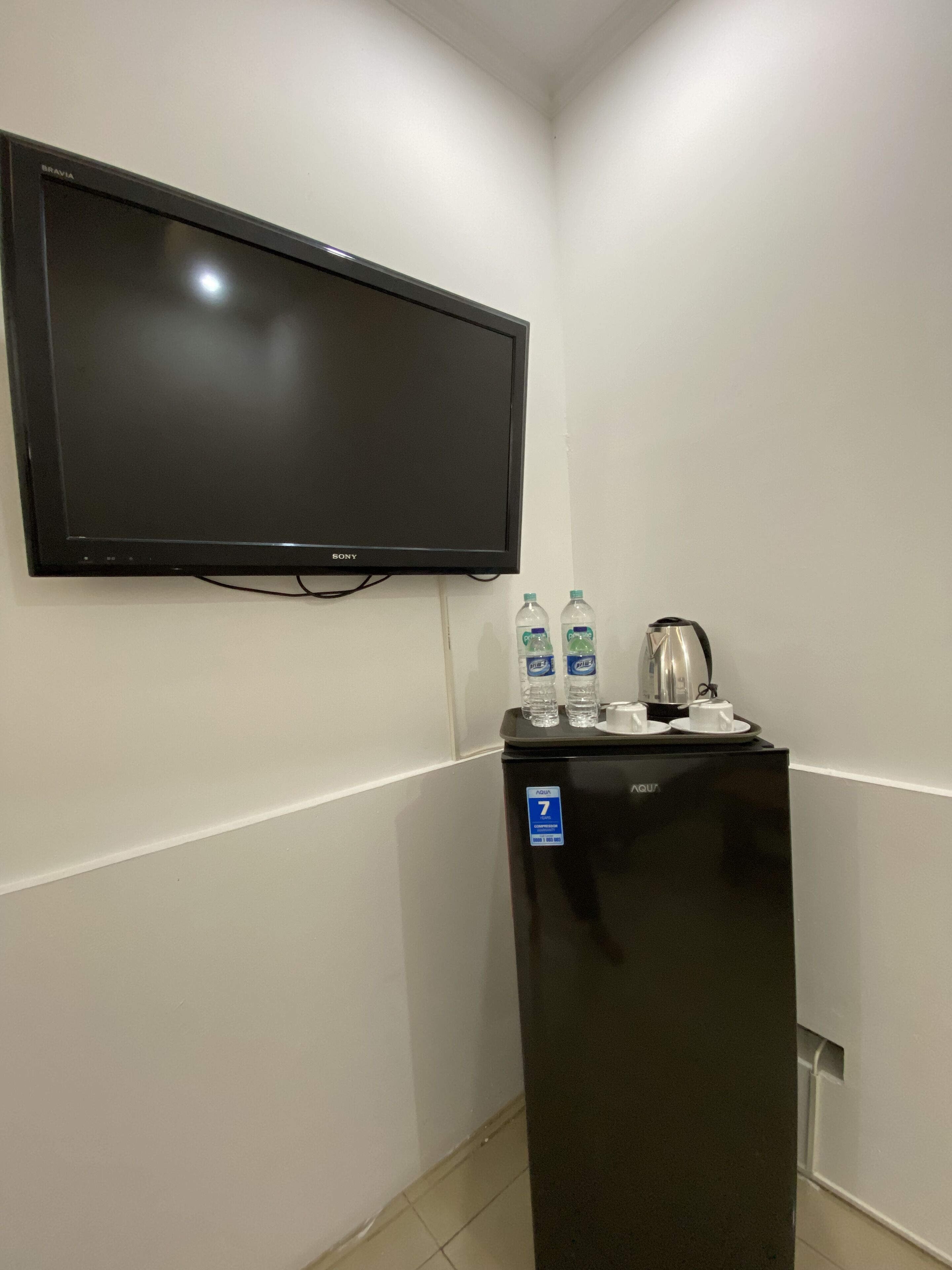Una habitación con televisión de pantalla plana en la pared, un refrigerador con dispensador de agua y una tetera encima.