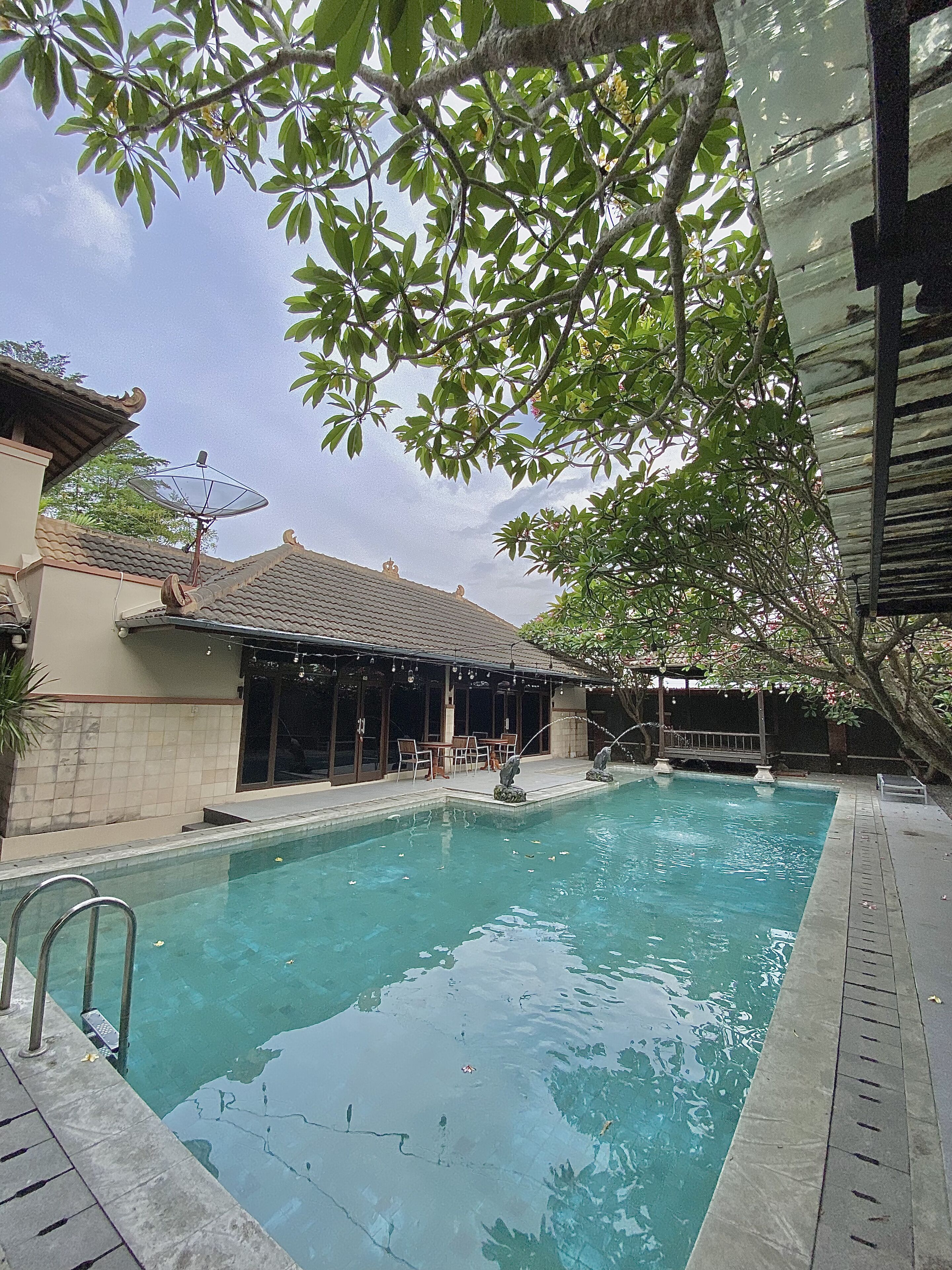 A swimming pool with a tiled deck, a covered seating area with tables and chairs, and a satellite dish on the roof.