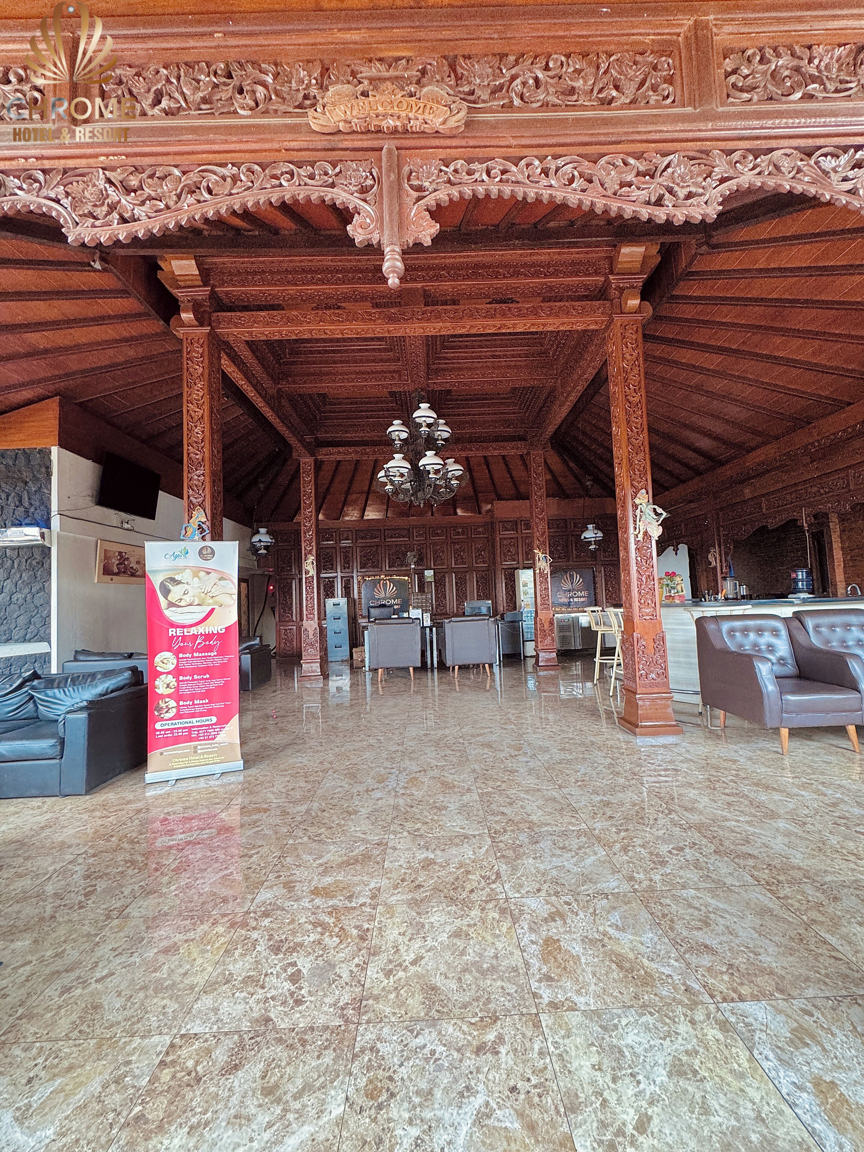 A hotel lobby with ornate wooden pillars, a reception desk, and a chandelier.