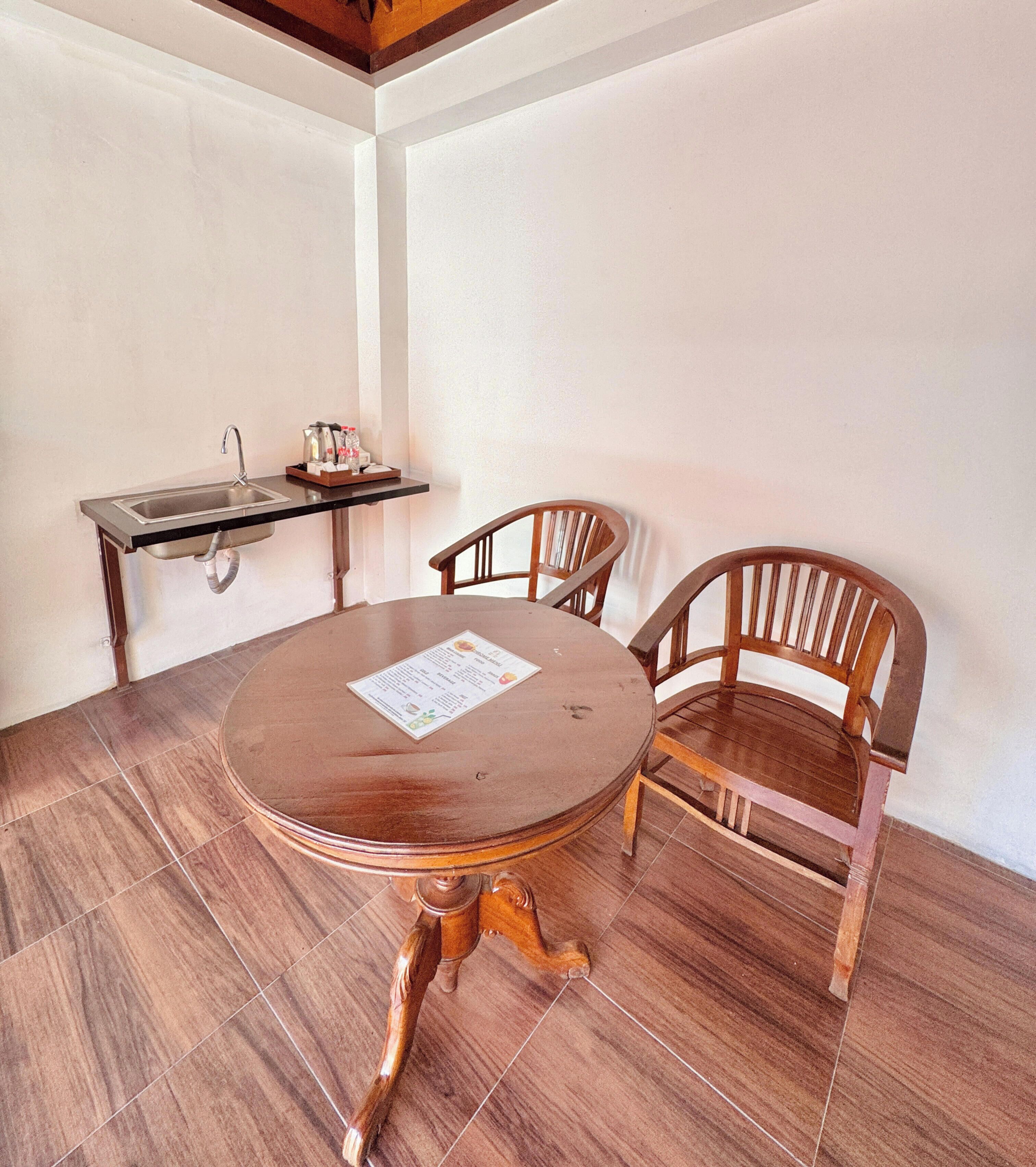 Uma área de refeições com uma mesa de madeira redonda, duas cadeiras de madeira, um pequeno bar com uma pia e um cardápio sobre a mesa.