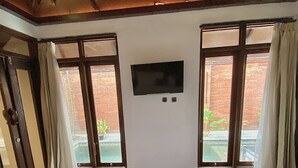 Habitación de hotel con una cama grande, un televisor de pantalla plana en la pared y ventanas amplias con cortinas.