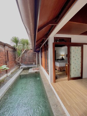 A pool area with a wooden deck, a brick wall, and a door leading to a bedroom. - Chrome Hotel & Resort Solo (Colomadu)