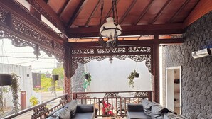 Un espacio de estar al aire libre techado con sofás de cuero negro, una mesa de centro de madera y plantas colgantes.