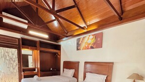 A hotel room with two beds, wooden ceiling beams, a wooden nightstand with a lamp, and a painting on the wall. - Chrome Hotel & Resort Solo (Colomadu)