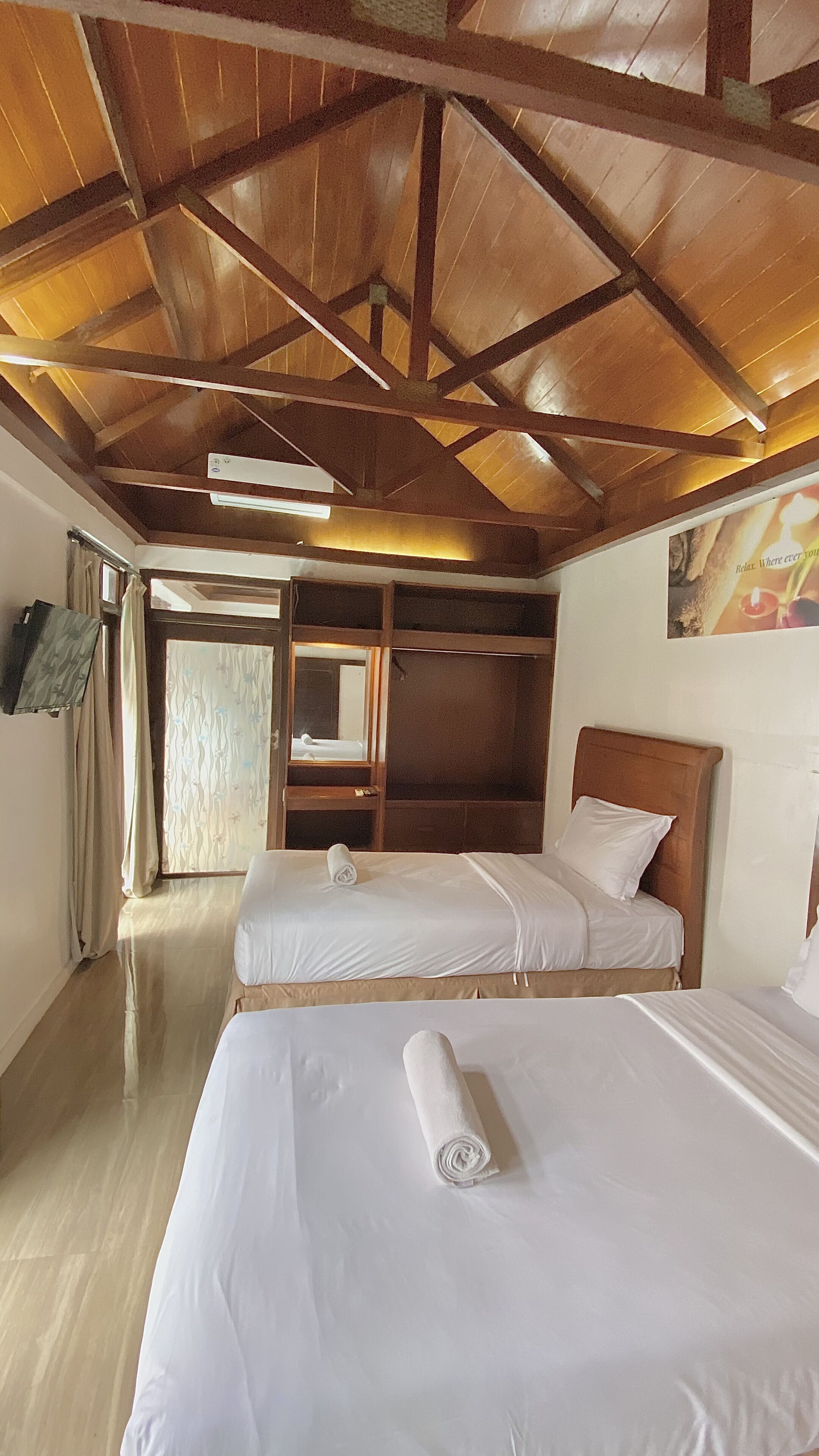 A hotel room with two beds, wooden ceiling beams, a large mirror, and a view of the outside.