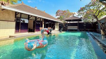 Una piscina con un flotador de flamenco, rodeada de edificios con techos de tejas y zonas de estar al aire libre.