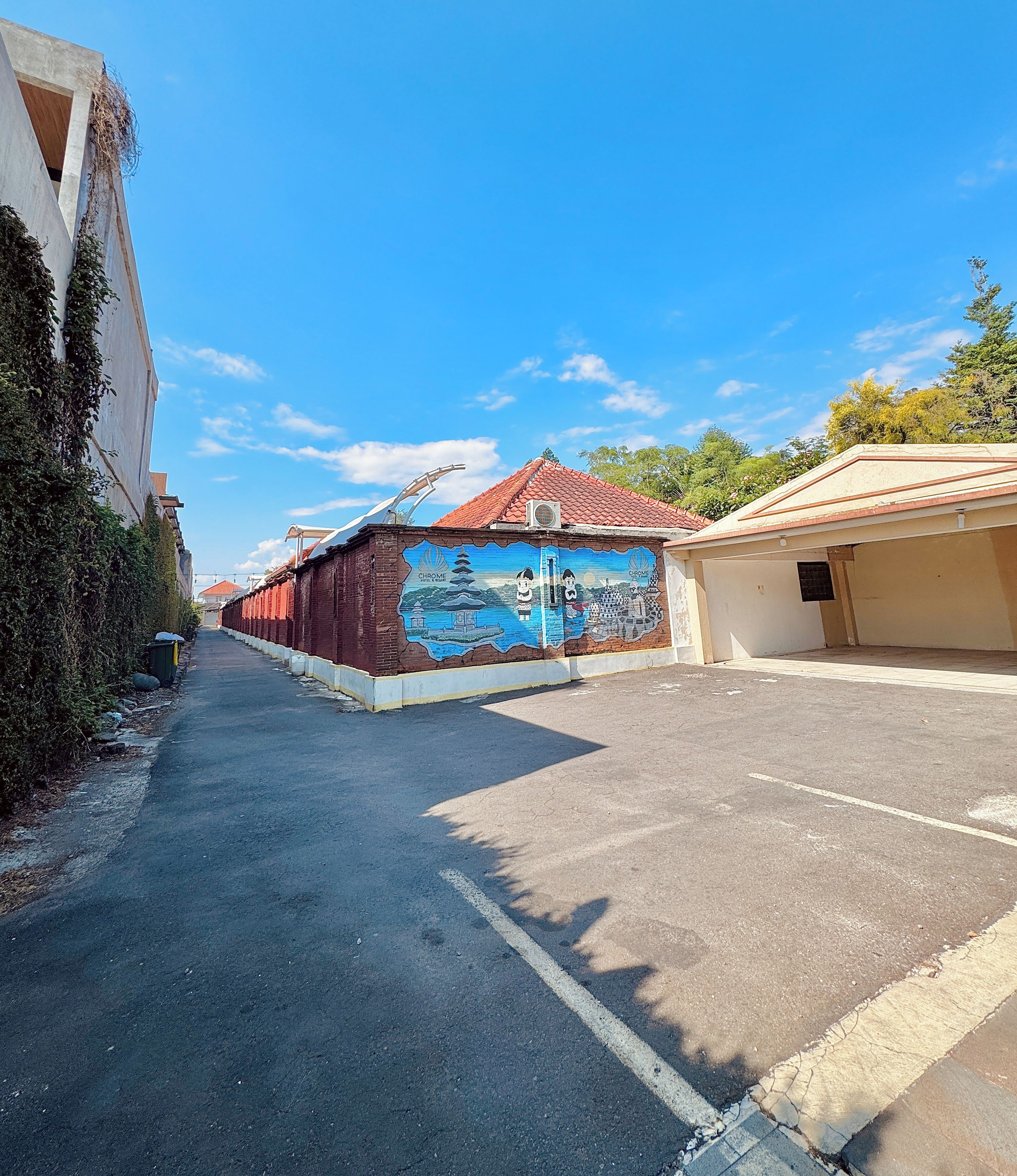 A street view with a building featuring a mural, a parking lot, and a clear blue sky.