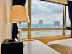 A hotel room with a bed, a bedside table with a lamp, and a window with a city view. - We Meet Taipei Hotel (New Taipei City)