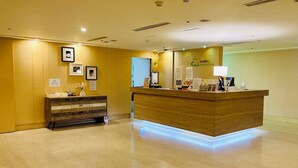 A reception area with a wooden reception desk, a small console table with decorative items, and framed pictures on the wall. - We Meet Taipei Hotel (New Taipei City)
