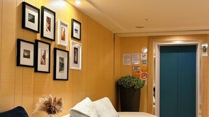 A hotel lobby with a sofa, a small table, and a wall decorated with framed photos. - We Meet Taipei Hotel (New Taipei City)
